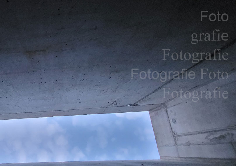 Aufblick an einer Wand entlang in den leicht bewölkten Himmel.